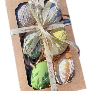 Set of 6 hand-painted Easter eggs in soft pastel green, grey, yellow and beige tones with white botanical line art, gold details and pearl dots