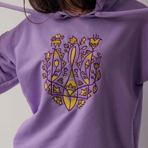 May include: A purple hoodie with a yellow and green embroidered design of stylized flowers and leaves.