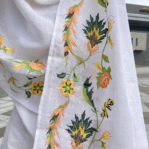 May include: White sheer scarf with embroidered floral design in shades of green, yellow, and orange.