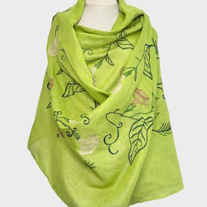 May include: A bright lime green scarf with embroidered floral and leaf patterns. The scarf is draped, highlighting the detailed embroidery of flowers and leaves. This lightweight scarf is a stylish accessory.