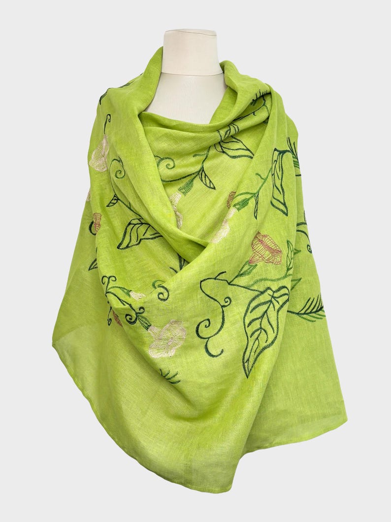 May include: A bright lime green scarf with embroidered floral and leaf patterns. The scarf is draped, highlighting the detailed embroidery of flowers and leaves. This lightweight scarf is a stylish accessory.