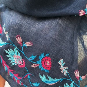 May include: A navy blue scarf with embroidered floral designs in shades of pink, red, and turquoise.