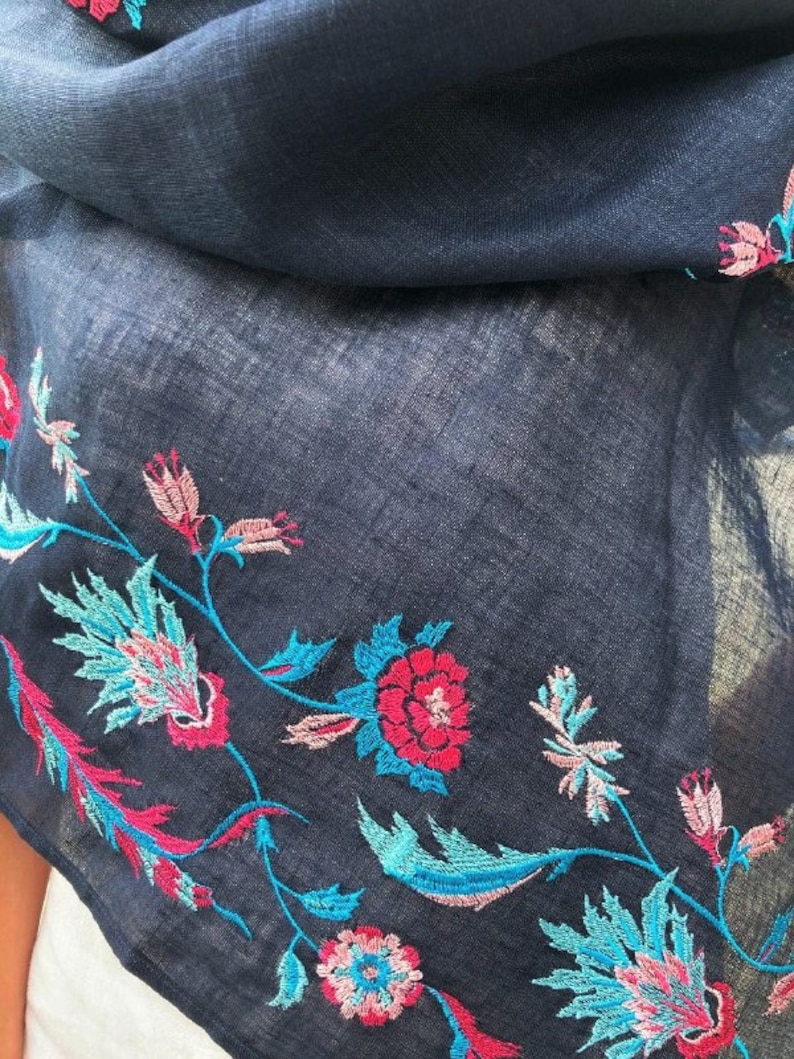 May include: A navy blue scarf with embroidered floral designs in shades of pink, red, and turquoise.