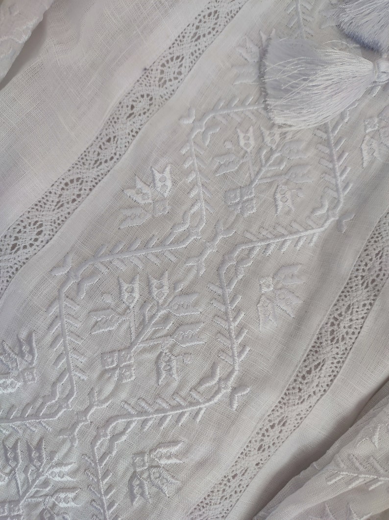 Peut inclure: Tissu de lin blanc avec un d&eacute;licat motif brod&eacute; blanc pr&eacute;sentant des formes g&eacute;om&eacute;triques et des motifs floraux. Le tissu est bord&eacute; d'une dentelle.