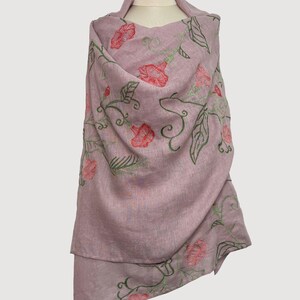 May include: A mauve shawl featuring embroidered red flowers and green leaves. The floral pattern adorns the shawl, displayed on a mannequin. The shawl is made from a soft, flowing material.