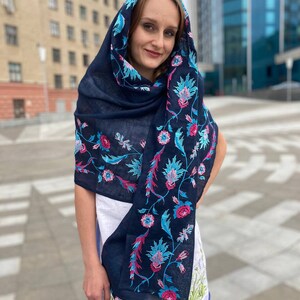 May include: A navy blue scarf with floral embroidery in pink, blue, and green. The scarf is draped over a person's head and shoulders.