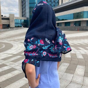 May include: A navy blue scarf with a floral pattern in pink, blue, and white. The scarf is draped over a person's head and shoulders.