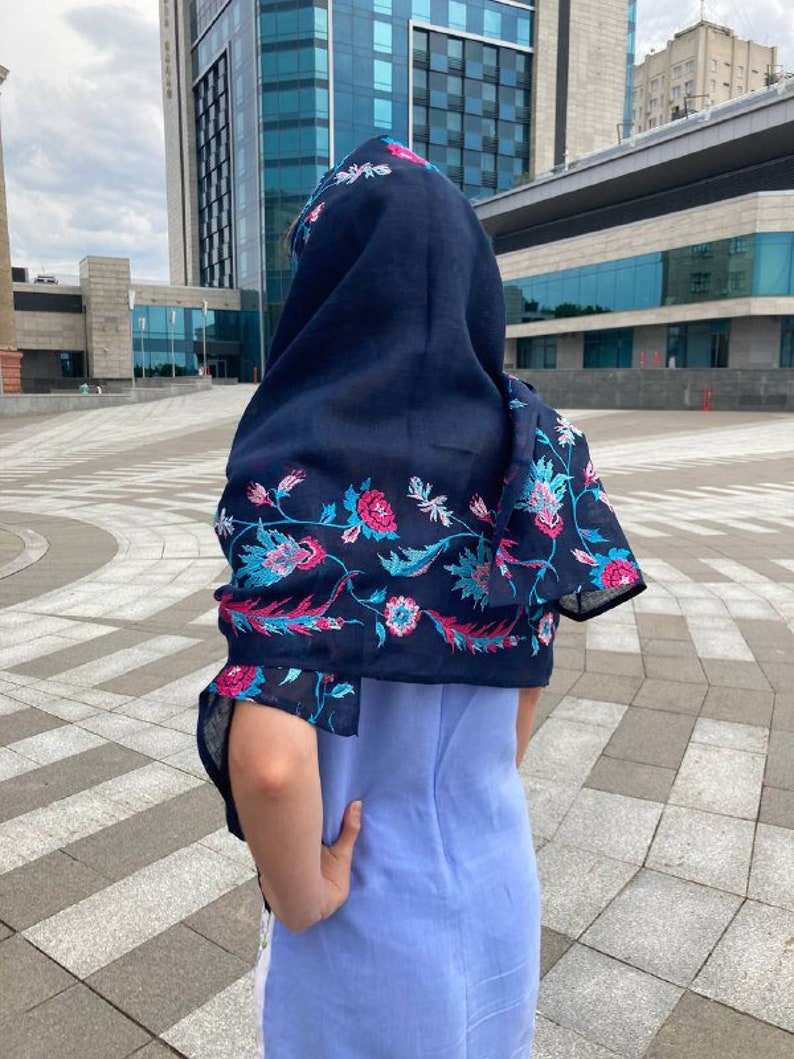 May include: A navy blue scarf with a floral pattern in pink, blue, and white. The scarf is draped over a person's head and shoulders.