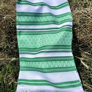 May include: White fabric with green embroidered stripes. The fabric has a fringe edge.
