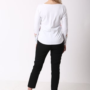 May include: A white long-sleeved top with floral embroidery on the sleeves, worn with black trousers and black high heels. The outfit is simple and elegant, suitable for various occasions.