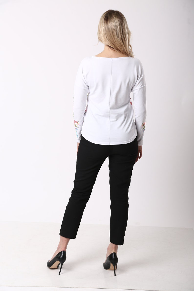 May include: A white long-sleeved top with floral embroidery on the sleeves, worn with black trousers and black high heels. The outfit is simple and elegant, suitable for various occasions.