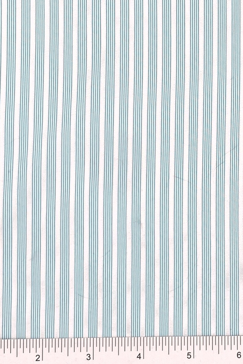 Puede incluir: Tela blanca con finas rayas azules claras espaciadas uniformemente. Una regla es visible en la parte inferior de la imagen, mostrando medidas en pulgadas.