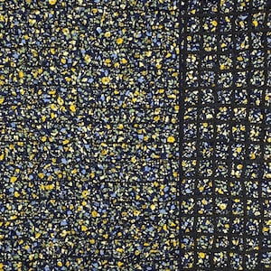 May include: Close-up of a fabric with a floral pattern. The pattern features small yellow, blue, and green flowers on a dark navy blue background. A section of black, grid-like netting is on the right side of the image.