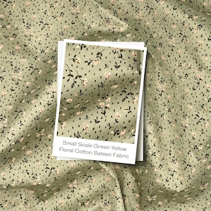 May include: Green and yellow floral cotton sateen fabric with a small-scale pattern. The fabric features tiny white flowers and dark green leaves on a light green background. The image includes a sample card with the fabric's description.