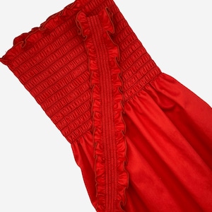 May include: A vibrant red strapless top with a shirred bodice and ruffled trim. The fabric has a slight sheen, and the design features a fitted, elasticized upper section. The overall style is summery and feminine.