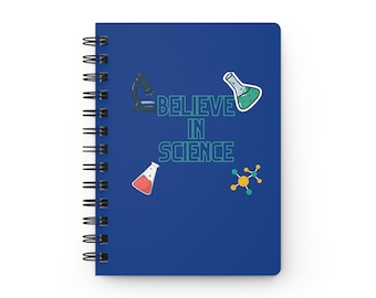 Może przedstawiać: Spiralny notatnik w kolorze granatowym z napisem "BELIEVE IN SCIENCE" w kolorze zielonym i białym. Okładka zawiera ilustracje mikroskopu, kolb i cząsteczki. Idealny dla miłośników nauki.