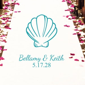 May include: A white aisle runner with pink flower petals on the sides. A teal blue seashell graphic is centered on the runner with the text "Bellamy & Keith 5.17.28" below it.