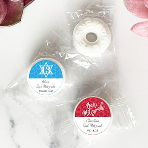 May include: Two clear plastic bags with round, white mints inside. One mint has a blue and white sticker with a Star of David and the text "Alex's Bar Mitzvah Thank you!" The other mint has a red and white sticker with the text "Bar Mitzvah Claudia's Bat Mitzvah 06.18.25"