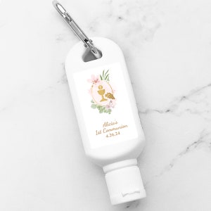 May include: White hand sanitizer bottle with a silver carabiner clip. The label features a gold chalice and grapes design with pink flowers and the text "Alicia's 1st Communion 4.26.24".
