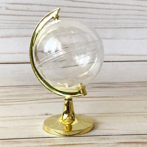 May include: A gold globe-shaped decorative container with a clear plastic globe. The globe is on a gold stand with a round base.