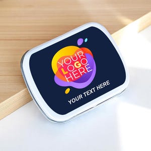 May include: A white, rectangular tin with a navy blue lid. The lid features a colorful logo design with the text "YOUR LOGO HERE" and "YOUR TEXT HERE". The tin is likely used for small items or promotional purposes.