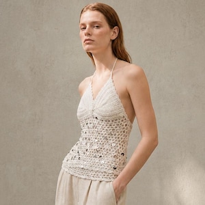 Pode incluir: Um top halter creme com design de crochê e lantejoulas, combinado com calças de linho bege. O conjunto é completado com sandálias castanhas. A roupa é adequada para climas quentes e ocasiões casuais.