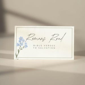 Op de afbeelding: Een rechthoekige kaart met de tekst "Romans Road" in sierlijke letters, met de zin "Bible Verses to Salvation" eronder. Een aquarel illustratie van blauwe bloemen siert de linkerkant. De kaart heeft een crèmekleurige achtergrond.