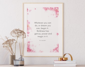May include: A framed print with the quote "Whatever you can do, or dream you can, begin it." in black text. Pink floral accents decorate the white background. The frame is light brown. The print is displayed on a wooden surface.