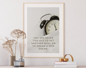 May include: A framed print with a black alarm clock and the text "YOU ARE NEVER TOO OLD TO SET ANOTHER GOAL OR TO DREAM A NEW DREAM."