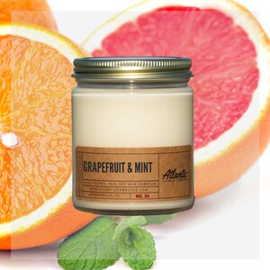 May include: A glass jar candle with a gold lid and a brown label that reads "GRAPEFRUIT & MINT" and "HAND-POURED 100% SOY WAX CANDLES" with the company name "Atlantic Candle Company" and website address "www.atlanticcandleco.com". The candle is surrounded by slices of grapefruit and mint leaves.
