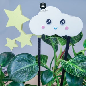 May include: A white cloud with a smiling face and pink cheeks, with three yellow stars on sticks, in front of a green plant.