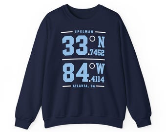 May include: A navy blue long-sleeve sweatshirt featuring light blue text and graphics. The design displays the word SPELMAN above coordinates 33°N .7452 and 84°W .4114, with the text ATLANTA, GA at the bottom, all framed by horizontal white lines.