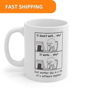 May include: White ceramic mug featuring a humorous comic strip about a software engineer's daily struggles. The text reads "It doesn't work... why?" and "It works... why?" with the phrase "Just another day in a life of a software engineer."