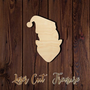 May include: A laser-cut wooden elf head shape with a hat and beard. The unfinished wood elf head is set against a dark brown wooden background. The words "Laser Cut Treasure" are written in a decorative font.