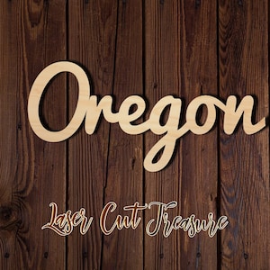 May include: Wooden cutout of the word "Oregon" in a cursive font. The cutout is on a brown wood background with the text "Laser Cut Treasure" below it.