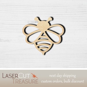 May include: A wooden cutout of a bee in a simple, stylized design. The bee is light brown and has a black outline. The bee is facing to the right.