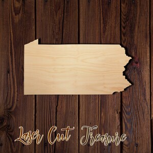 May include: Laser cut wooden cutout of the state of Pennsylvania. The cutout is on a brown wood background. The text "Laser Cut Treasure" is written below the cutout.
