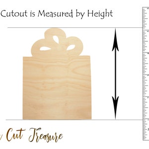 May include: A wooden cutout of a gift box with a bow on top. The cutout is approximately 5 inches tall. "This Cutout is Measured by Height" and "Laser Cut Treasure" are printed below the cutout.