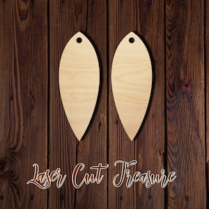 May include: Two unfinished wooden leaf-shaped ornaments with a hole at the top for hanging. The ornaments are on a brown wooden background.