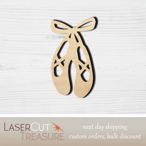 May include: Wooden cutout of a pair of ballet shoes tied together with a bow. The shoes are light brown and have a simple design.