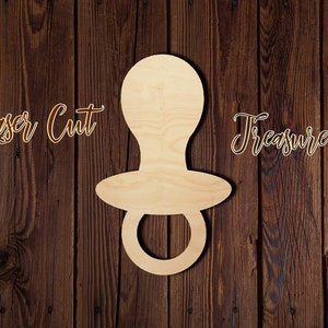 May include: A wooden cutout of a baby pacifier, with the words "Laser Cut Treasure" written on the background.