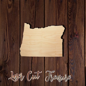 May include: Laser cut wooden cutout of the state of Oregon on a brown wood background. The text "Laser Cut Treasure" is written below the cutout.