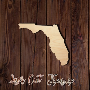 May include: Laser cut wooden outline of the state of Florida on a brown wood background. The text "Laser Cut Treasure" is written below the state outline.