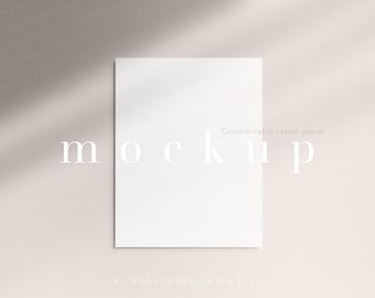May include: A blank white rectangular sheet of paper positioned in the centre. The word mockup is printed in large white letters across the middle, with the text Customizable Letter paper appearing in a smaller font above the word mockup.