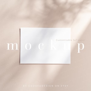 Op de afbeelding: Een witte 5x7 inch papieren mockup op een lichtbeige achtergrond met een schaduw van een plant. De tekst "mockup" is in wit op het papier gedrukt. De tekst "Customizable 5x7 paper" is in wit op het papier gedrukt. De tekst "BY DODDUFODESIGN ON ETSY" is in wit onderaan de afbeelding gedrukt.