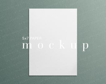 May include: A white 5x7 inch (approx. 13 x 18 cm) paper mockup against a textured teal background. The word "mockup" is displayed in a minimalist font. The text "5x7 PAPER" is above the word "mockup". The Etsy shop name "BY DODUFODESIGN ON ETSY" is at the bottom.