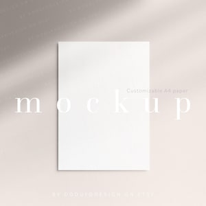Puede incluir: Una maqueta de papel A4 blanco en blanco centrada en el marco. El papel tiene una textura lisa y mate y está colocado verticalmente. La palabra mockup está impresa en letras minúsculas blancas con remates en el centro.