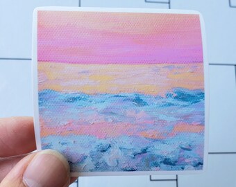 May include: A sticker with a painted image of a pink, yellow, and blue sunset over the ocean. The ocean is depicted with blue, white, and purple brushstrokes.