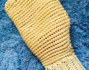 May include: A light yellow crocheted sleeve, possibly a wrist warmer or part of a garment, rests on a blue, fluffy surface. The sleeve has an open weave design and a ribbed knit cuff. The colour is a pale yellow.