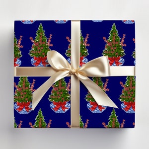 May include: A wrapped gift with navy blue wrapping paper featuring a repeating pattern of green Christmas trees in blue and white vases with red bows. The gift is tied with a cream-colored satin ribbon and bow.